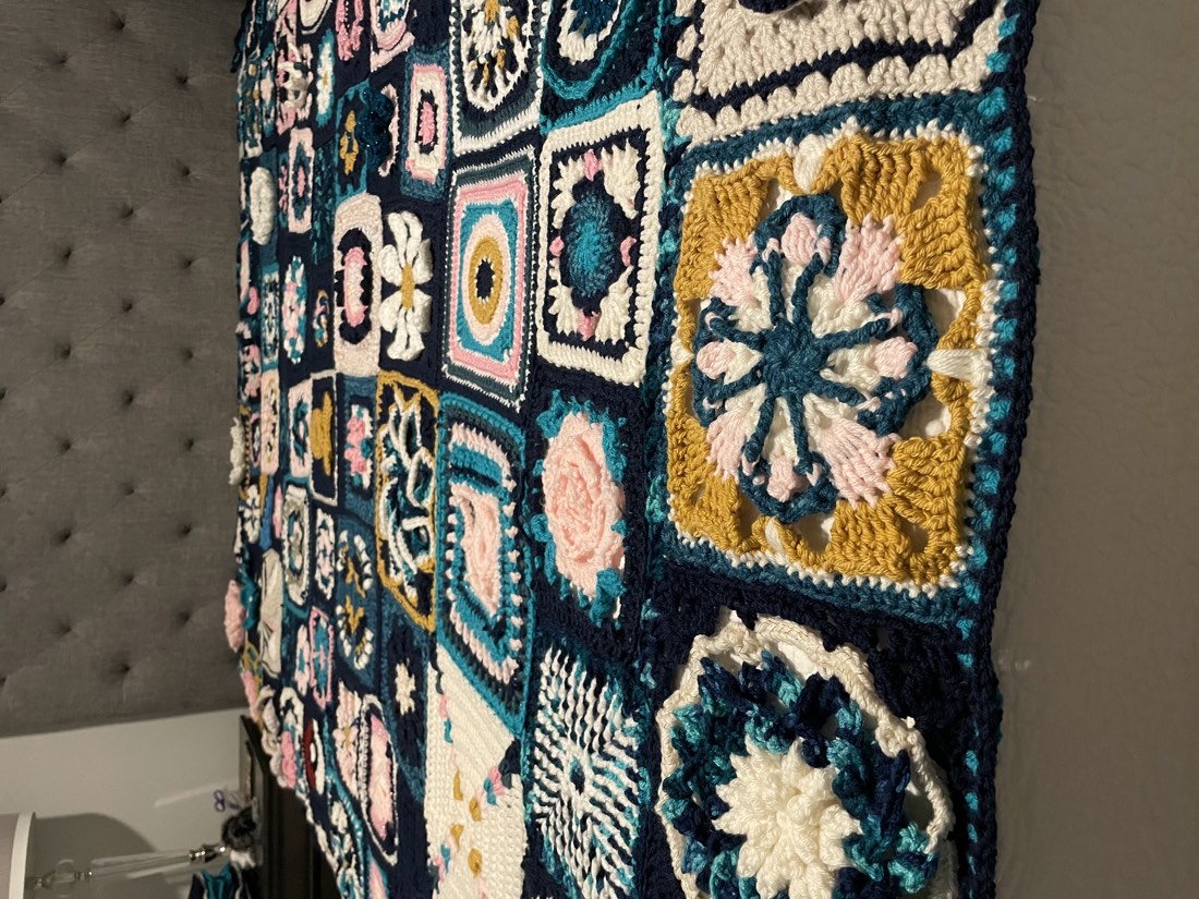 Crochet granny square blanket close-up, draped over a headboard, showing the variety of stitches and colors