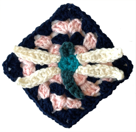 Crochet granny square with a raised dragonfly appliqué in cream and teal on a navy and pink background